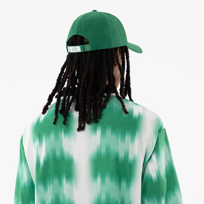 Boston Celtics NBA Green Soccer Jersey, back view on a model styled with long hair under a green cap, highlighting the jersey's white and green gradient pattern and the adjustable strap with a Celtics logo on the cap.
