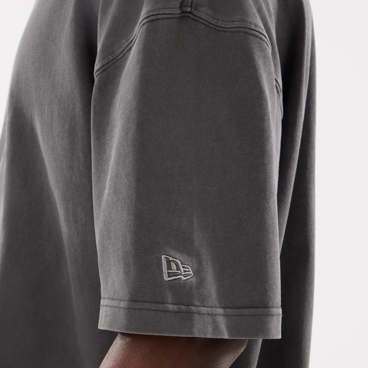 New Era Graphic Street Archived Washed Black Oversized T-Shirt, side view showing the washed black fabric with a raised New Era logo embroidered near the bottom of the short sleeve.