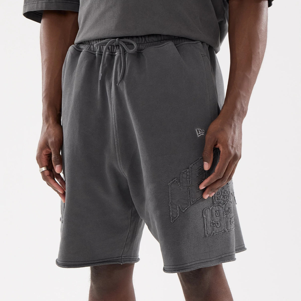 New Era Street Archived Black Oversized Shorts, front view showing a drawstring waist, the raised New Era logo on the left thigh, and large embossed lettering with "NYC 1920" on the right leg.