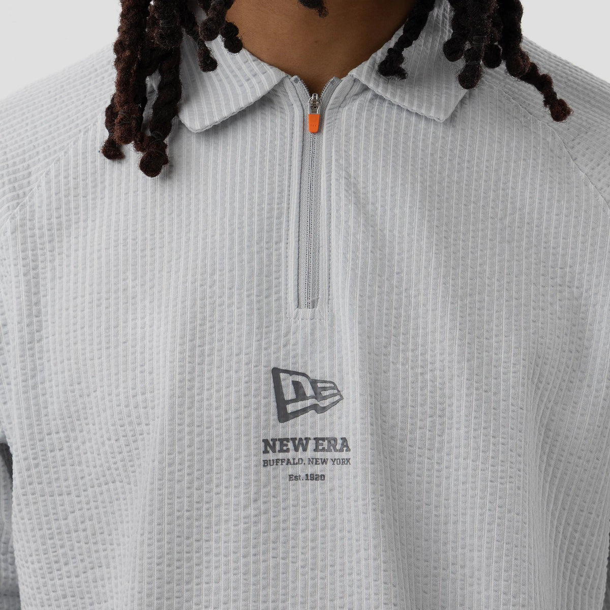 New Era Seersucker Grey Polo T-Shirt, front view showing a textured grey fabric with a quarter-length zip featuring an orange pull tab, a raised New Era logo printed centrally on the chest beneath the collar.