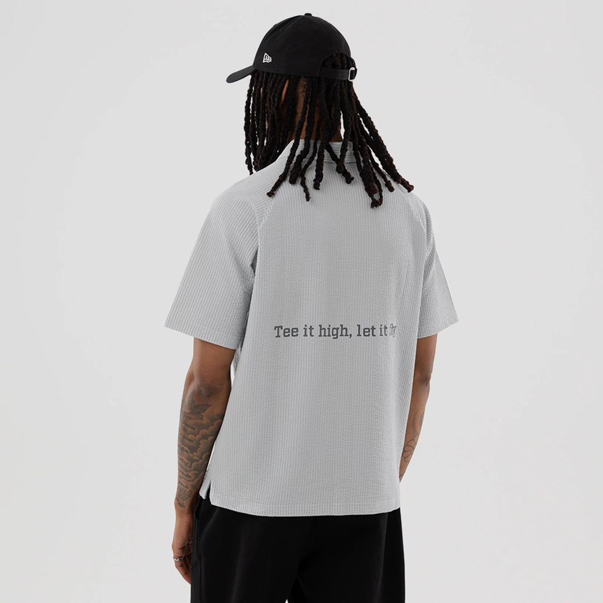 New Era Seersucker Grey Polo T-Shirt, rear view showing the light grey textured fabric with a printed slogan "Tee it high, let it fly" across the back, short sleeves, and a straight hem.