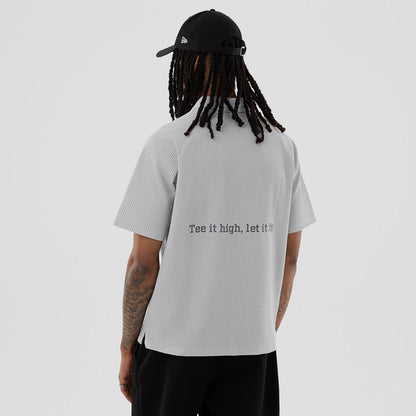 New Era Seersucker Grey Polo T-Shirt, rear view showing the light grey textured fabric with a printed slogan "Tee it high, let it fly" across the back, short sleeves, and a straight hem.