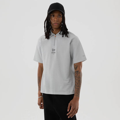 New Era Seersucker Grey Polo T-Shirt, on-model view featuring a light grey textured polo with a half zip and a raised New Era logo centred on the chest, short sleeves, and a casual fit worn by a person in black trousers.