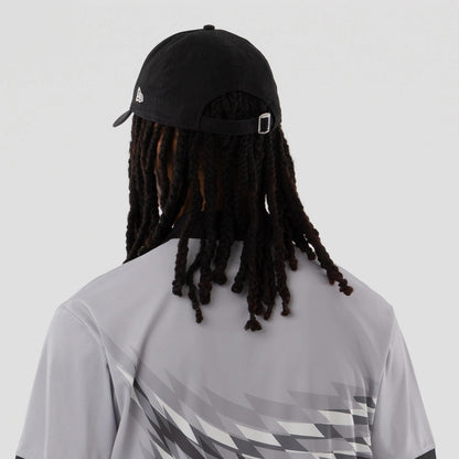 New Era Grid Grey Polo T-Shirt, on-model view featuring the grey polo with a geometric grid pattern across the back, paired with a black cap showing a raised New Era logo on the left side above the strap.