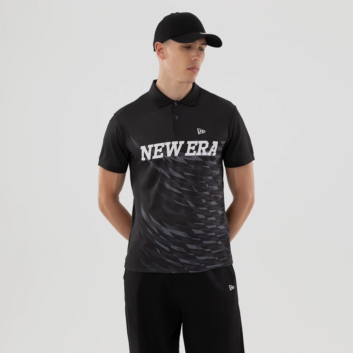 New Era Grid Black Polo T-Shirt, on-model view showing a man wearing the black polo with a white New Era text across the chest, a small raised logo on the left chest, and a grey grid pattern on the lower half.