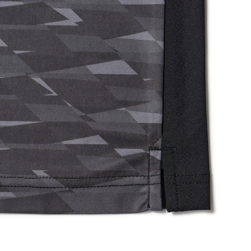 New Era Grid Black Polo T-Shirt, side view showing the bottom hem with a geometric black and grey pattern, a small slit detail at the seam, and contrasting black fabric on the right edge.