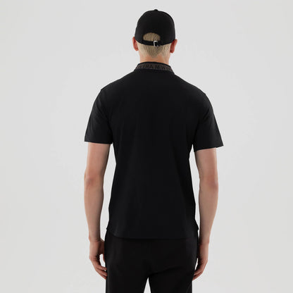 New Era Kanoko Black Polo T-Shirt, rear view showing a black collar with repeated debossed New Era text, short sleeves and a straight hem, worn by a person also wearing a black cap with an adjustable strap.