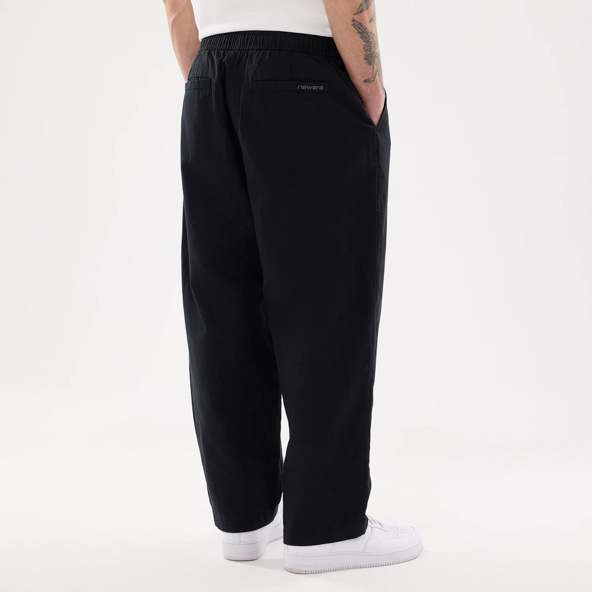 New Era Black Balloon Leg Trousers, rear view on a model wearing white trainers and a white top, showing the elasticated waistband and embroidered New Era logo above the right back pocket.