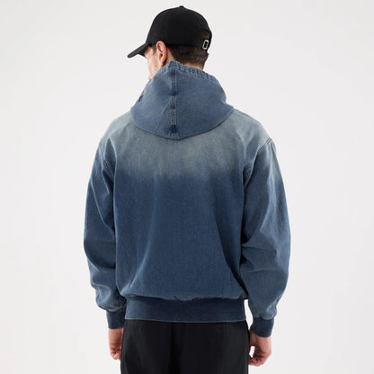 New Era Washed Blue Full Zip Hoodie, rear view showing the faded blue back with a hood, ribbed cuffs and hem, worn by a model in black trousers, and a black cap with a debossed logo on the back.