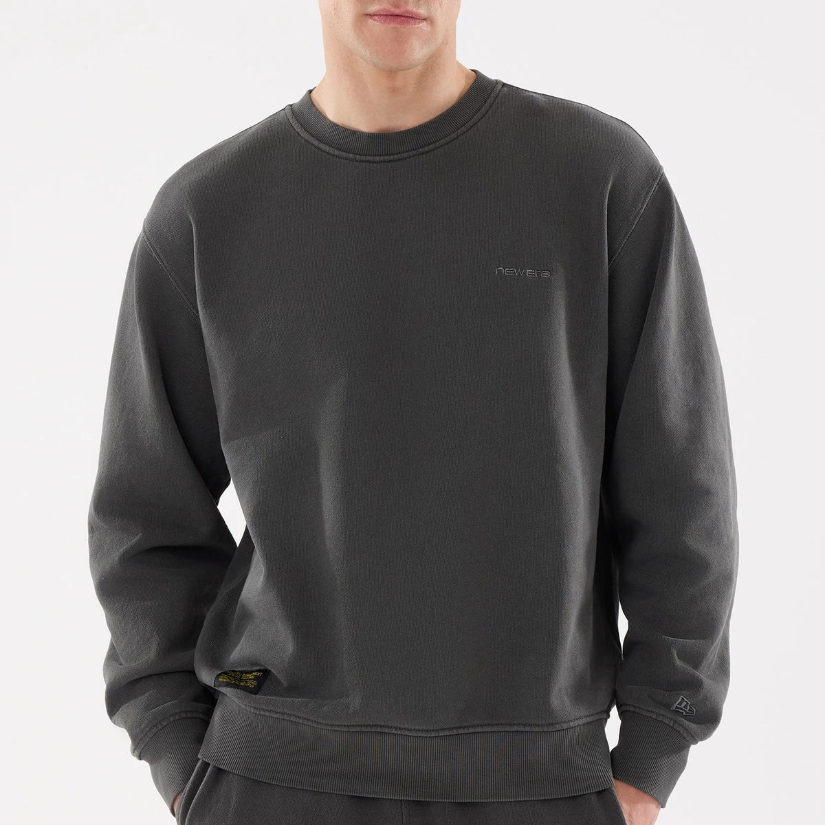 New Era Originators Black Crew Neck Sweater, front view on a model showing the subtle tonal New Era logo embroidered on the left chest, ribbed collar and cuffs, and a small black and gold tag above the waistband.