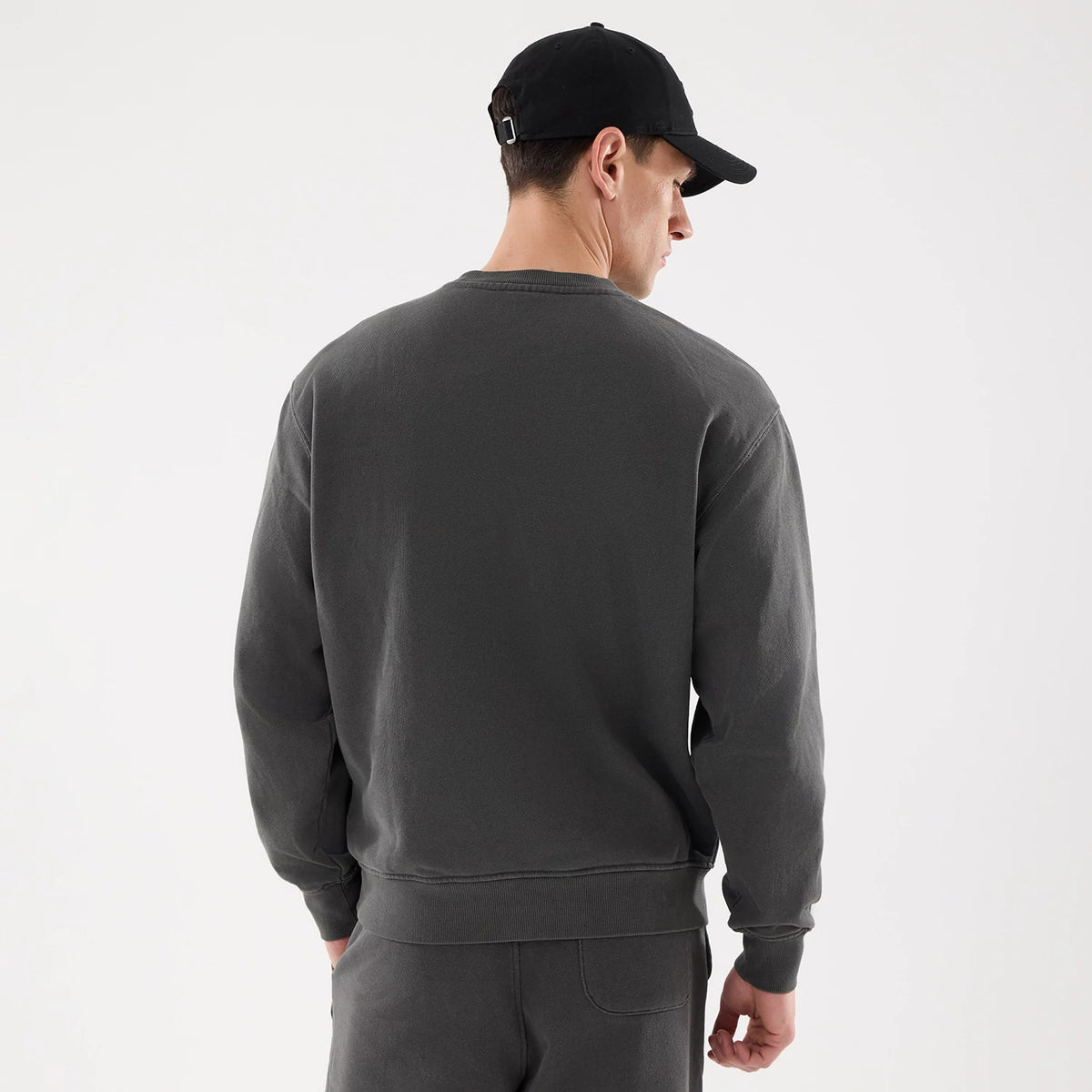 New Era Originators Black Crew Neck Sweater, back view on a model showing the plain black fabric and loose fit, paired with a black cap, highlighting the clean design and casual style.