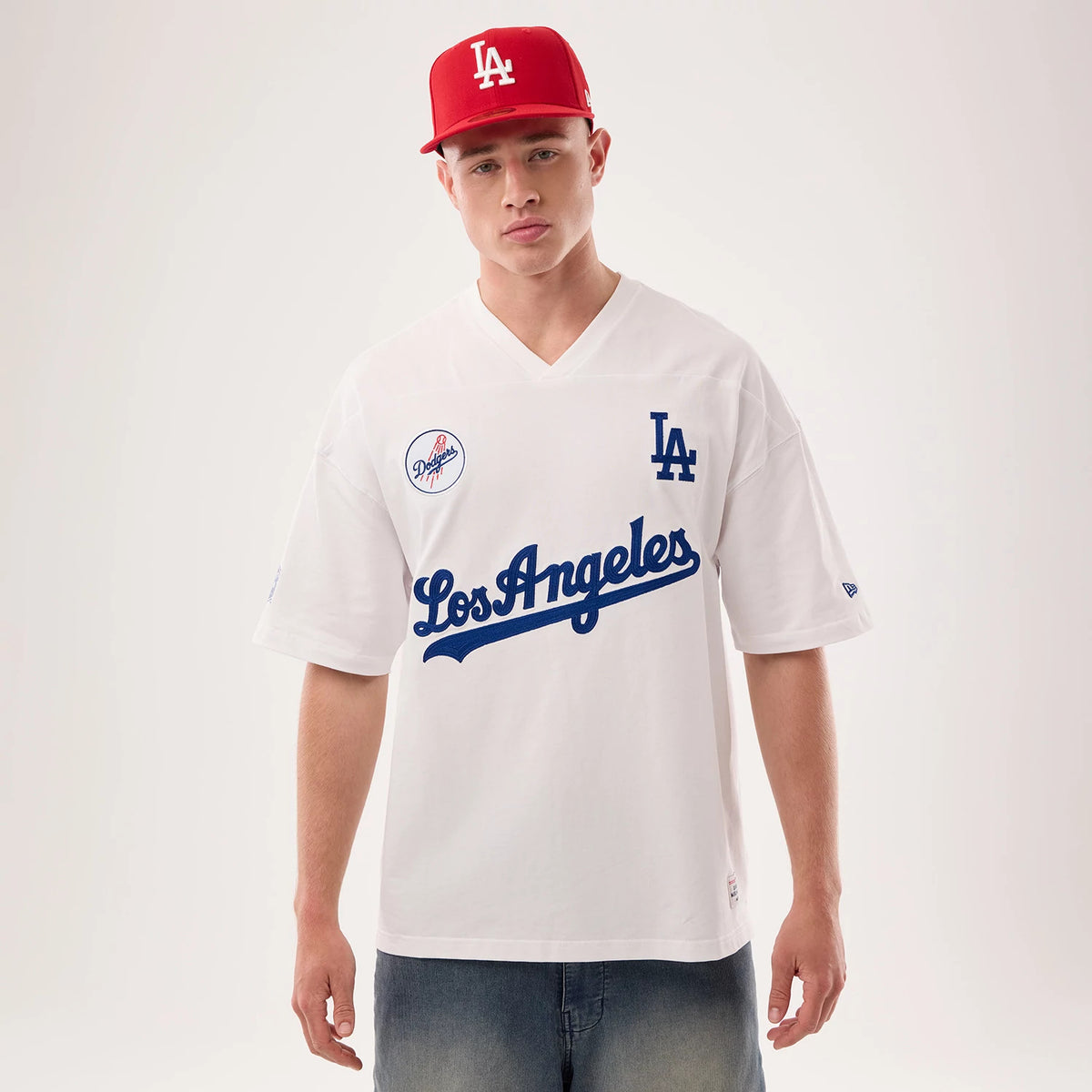 Los Angeles Dodgers MLB Fan Family White Jersey, front view on a model wearing a red cap, featuring a blue "Los Angeles" script across the chest, LA logo on the right side and a Dodgers patch on the left chest.