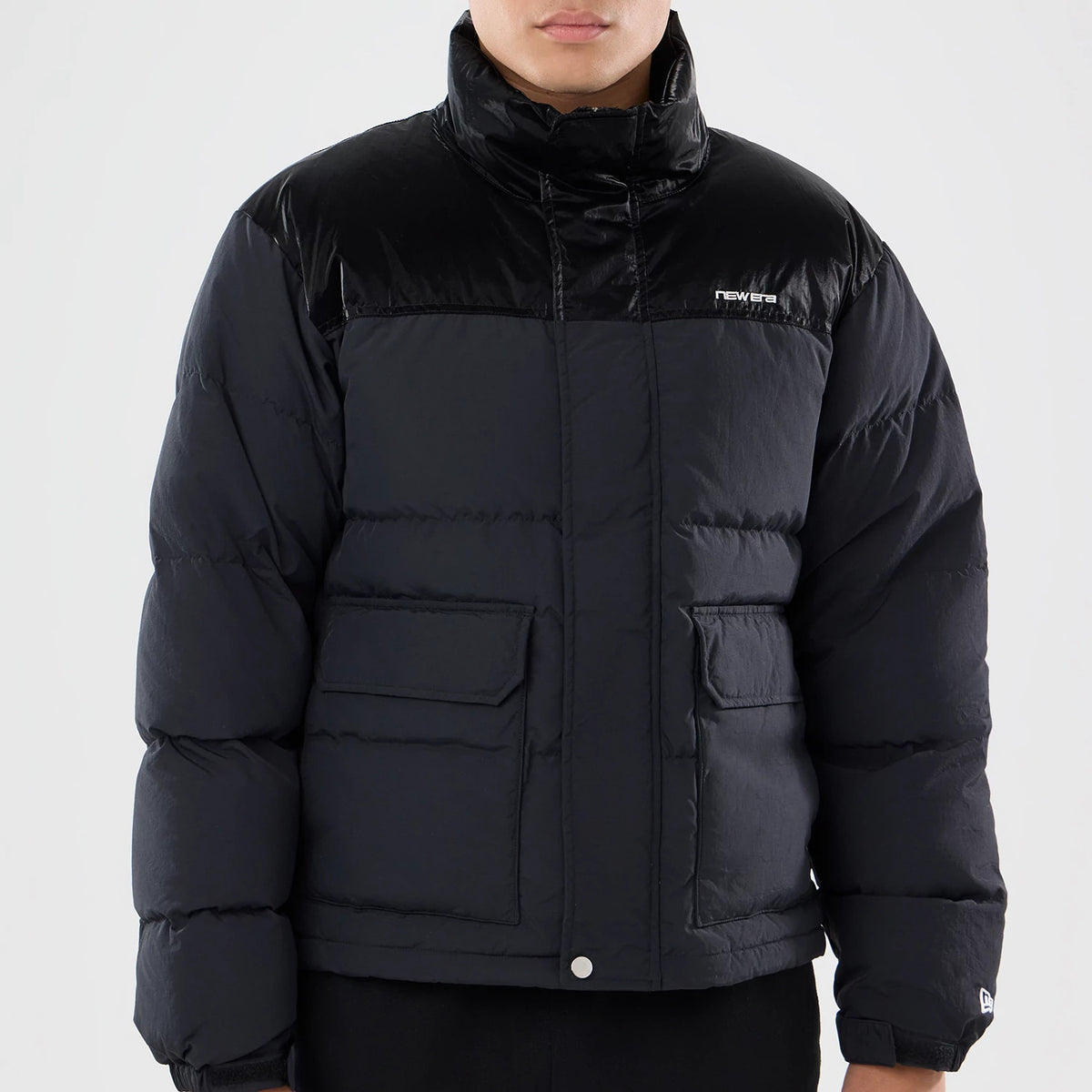 New Era Down Black Jacket, front view showing the padded black design with a raised New Era logo on the upper right chest, a high collar, buttoned flap pockets on each side, and long sleeves with a small logo on the left cuff.