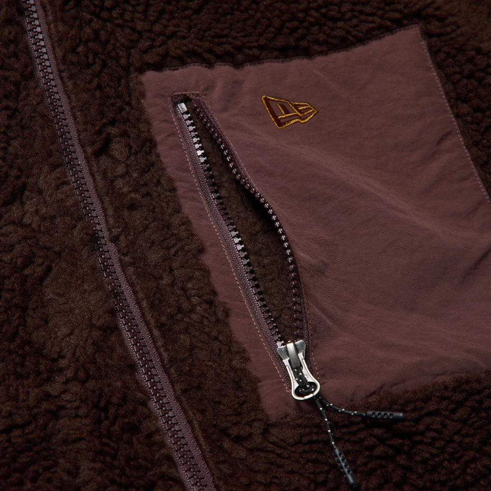 New Era Blouson Dark Brown Jacket, close-up view showing the dark brown textured fabric, a vertical zip on a pocket with a debossed New Era logo above, and another central zip on the left side.