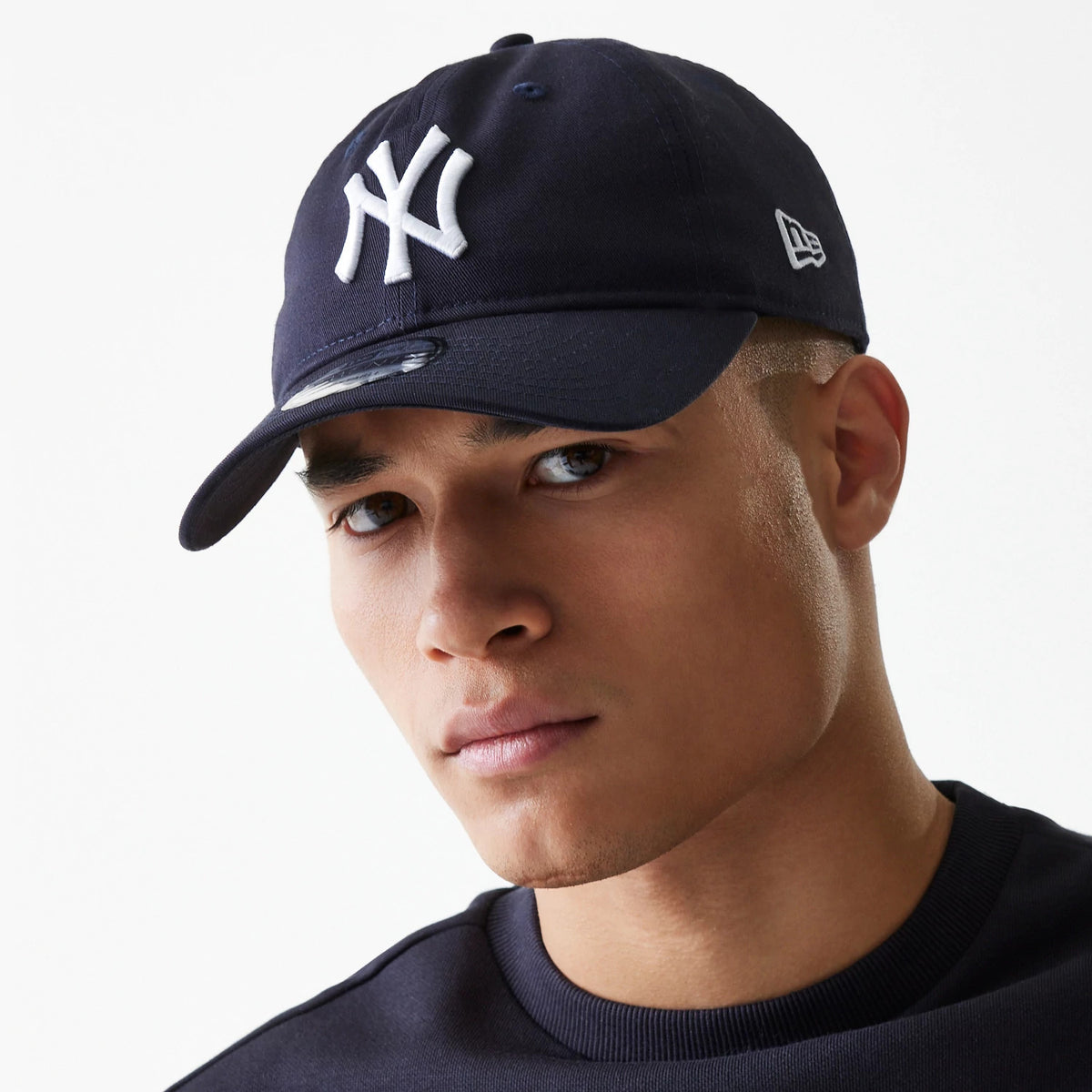 New York Yankees League Essential Navy New Era 9TWENTY Adjustable Cap, on-model front view with a white embroidered NY logo on the front panel, curved visor with a 9TWENTY size sticker, and a New Era flag logo on the left side.