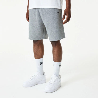 New Era Essential Grey Shorts, on-model view showing grey knee-length shorts with an embroidered New Era logo on the left leg, paired with white socks featuring a black New Era logo and white trainers.