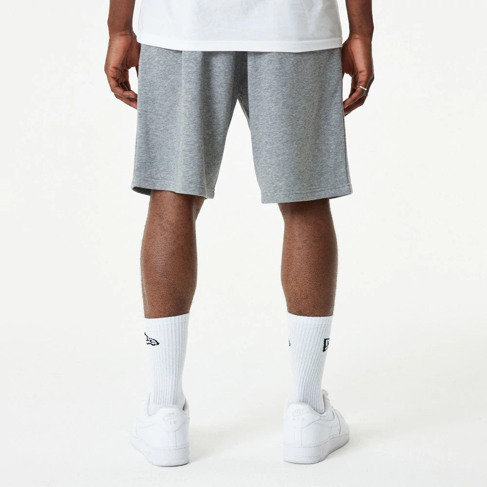 New Era Essential Grey Shorts, rear view showing a simple grey design with a straight hem, worn by a person standing with their back to the camera, complemented by white socks and trainers.