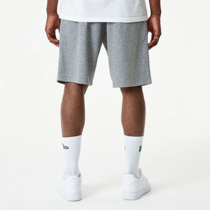 New Era Essential Grey Shorts, rear view showing a simple grey design with a straight hem, worn by a person standing with their back to the camera, complemented by white socks and trainers.
