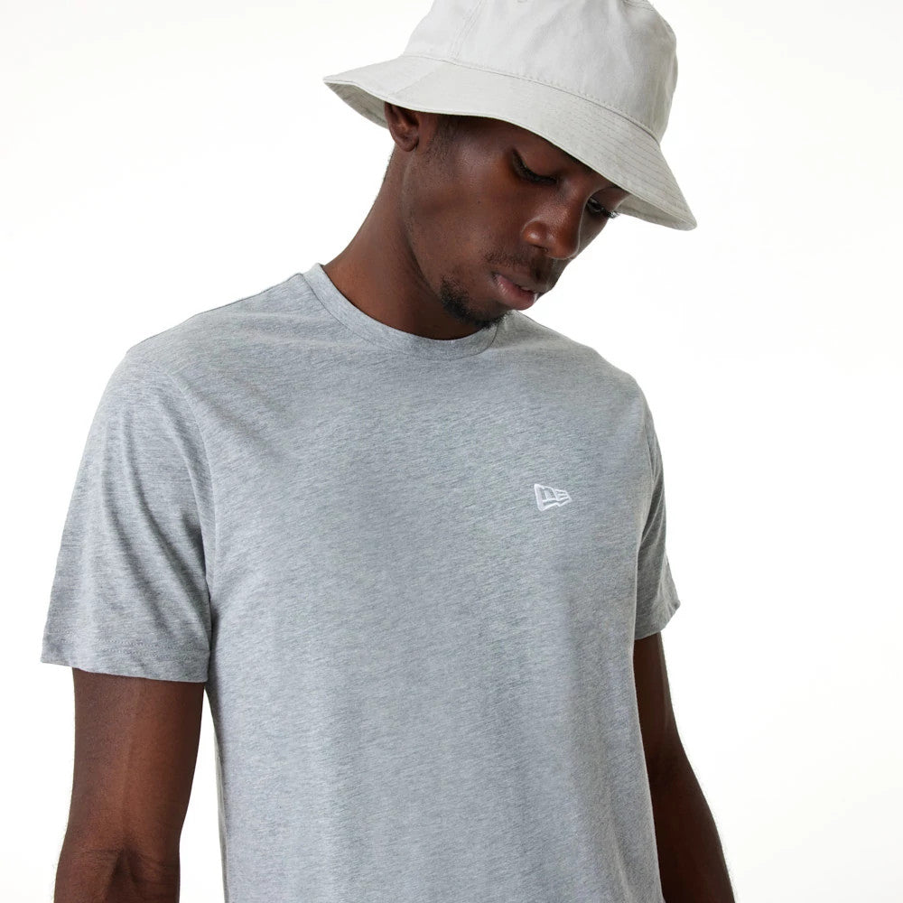 New Era Essential Grey T-Shirt, on-model view showing a pale grey short-sleeve design with a white embroidered New Era logo on the left chest, styled with a neutral bucket hat for a casual look.