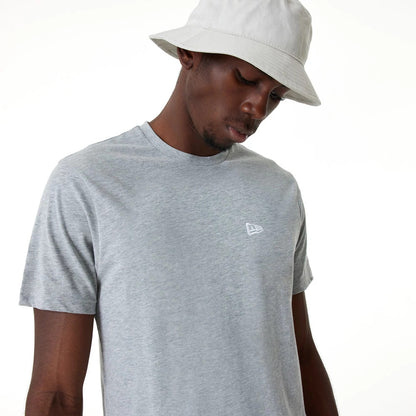 New Era Essential Grey T-Shirt, on-model view showing a pale grey short-sleeve design with a white embroidered New Era logo on the left chest, styled with a neutral bucket hat for a casual look.