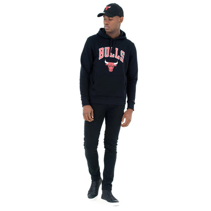 Chicago Bulls NBA Regular Black Pullover Hoodie, on-model view showing the black hoodie with bold red BULLS lettering and a bull logo on the chest, paired with black trousers and a black cap with an embroidered red bull logo.