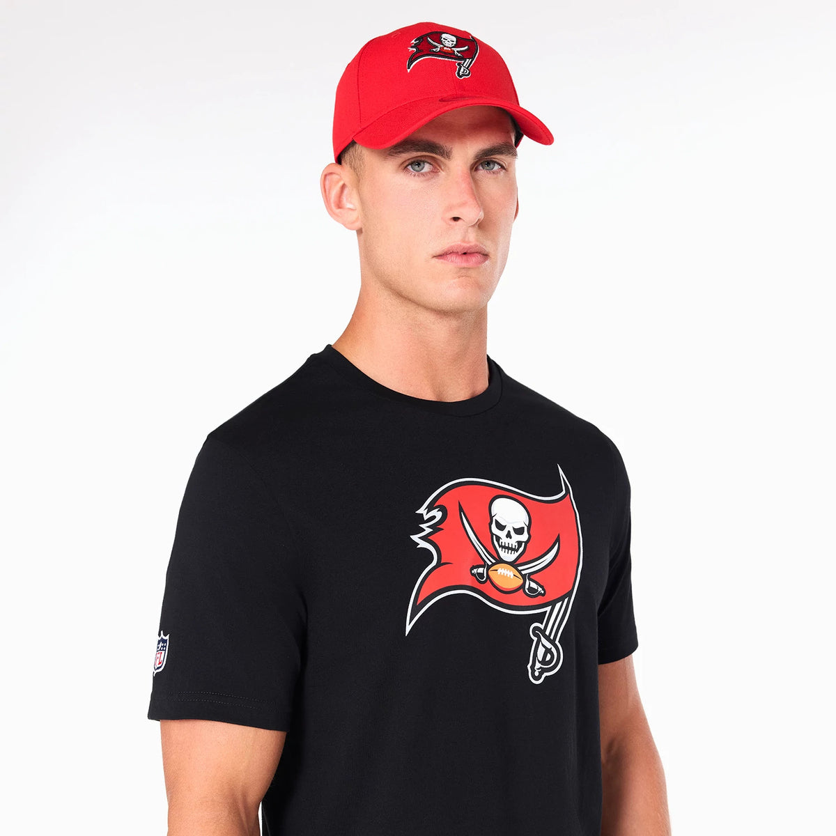 Tampa Bay Buccaneers NFL Black T-Shirt, on-model view showing a front graphic of a red pirate flag with a skull and crossed sabres logo on a black surface, and a red cap with the same debossed logo above the peak.