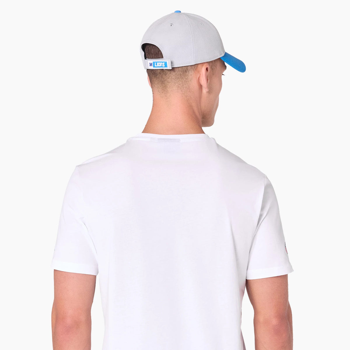 New Era Detroit Lions NFL White T-Shirt, rear view showing a plain white back with a grey cap featuring a blue brim and debossed logo on the rear tab, eyelets on the cap, worn by a model.