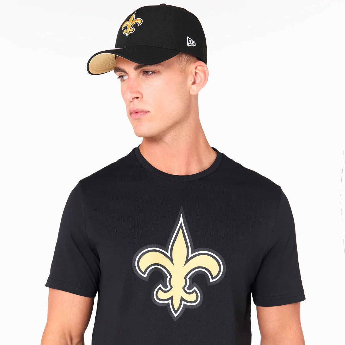 New Era New Orleans Saints NFL Black T-Shirt, on-model view showing the black T-shirt with a large gold fleur-de-lis emblem on the front and a black cap with an embroidered team logo worn by the model.