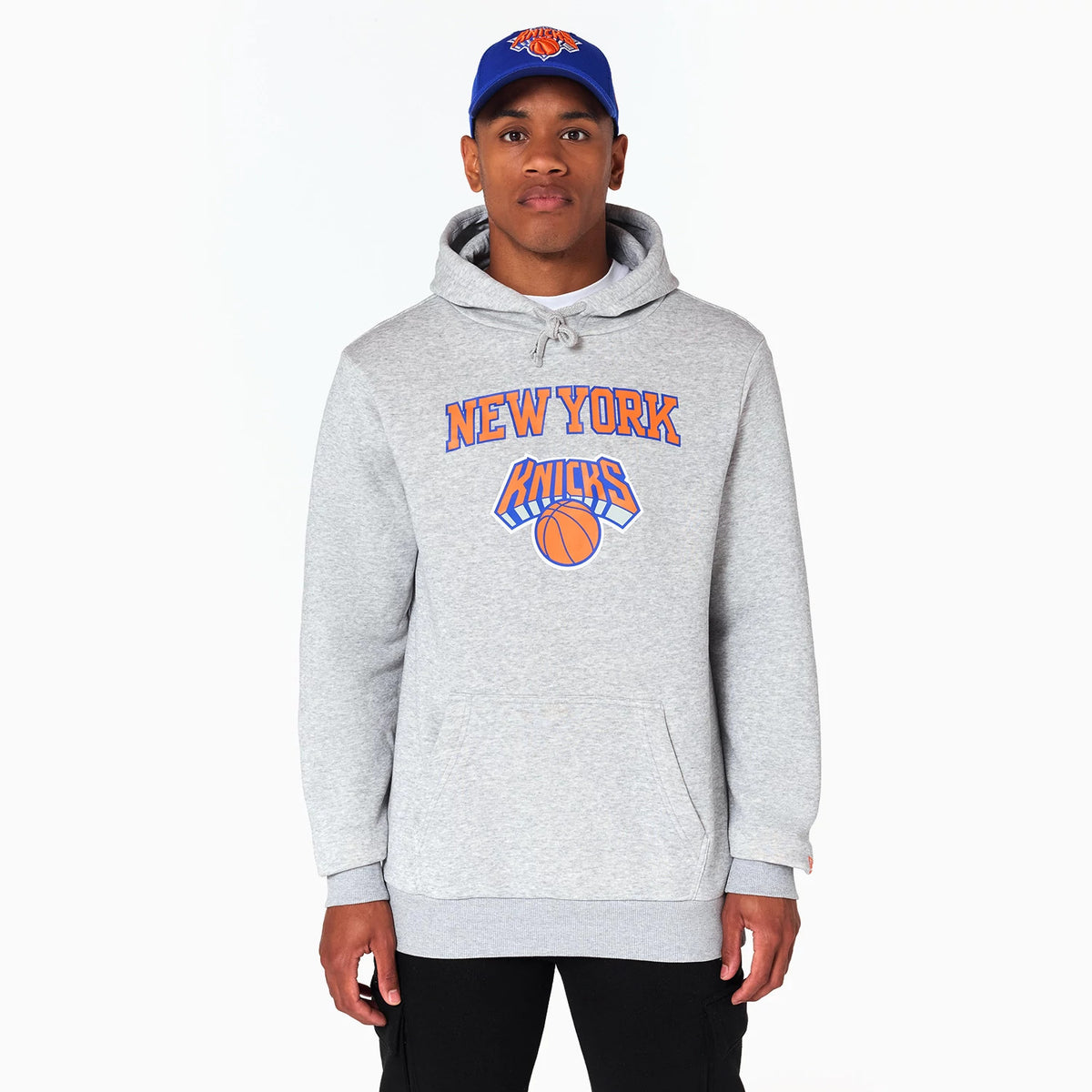 New Era New York Knicks NBA Grey Pullover Hoodie, front view showing the grey hoodie with a large front pocket, New York Knicks logo printed in orange and blue on the chest, worn by a model with a matching blue cap.