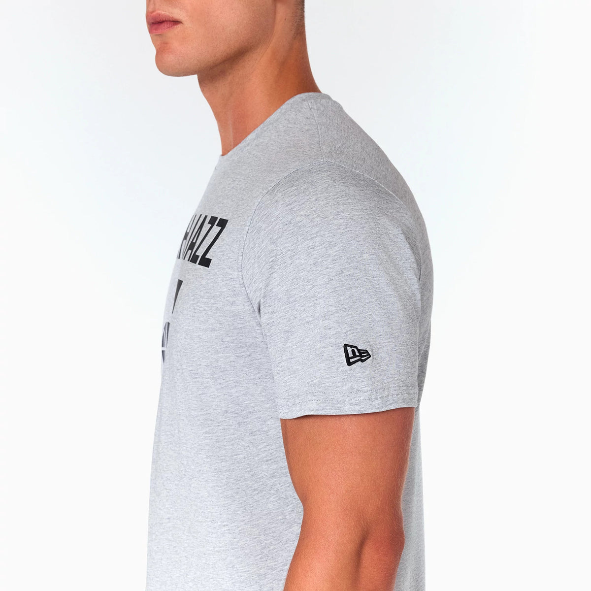 New Era Utah Jazz NBA Grey T-Shirt, side view showing the light grey fabric with a small raised New Era logo on the left sleeve and part of the bold Utah Jazz text design on the chest.