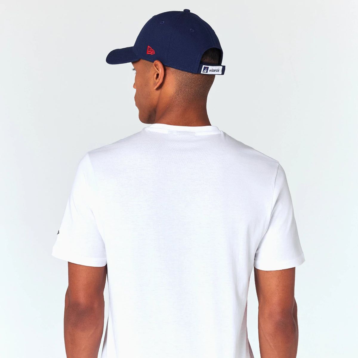 New Era Washington Wizards NBA White T-Shirt, on-model rear view showing a plain white back, person wearing a navy cap with a debossed red New Era logo on the side and an embroidered Wizards logo on the back strap.