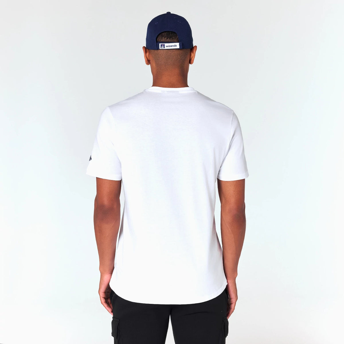 New Era Washington Wizards NBA White T-Shirt, on-model rear view showing a plain white back with the sleeves extending just above the elbows, a small raised logo on the left sleeve, and a blue cap with a Wizards logo at the centre back.