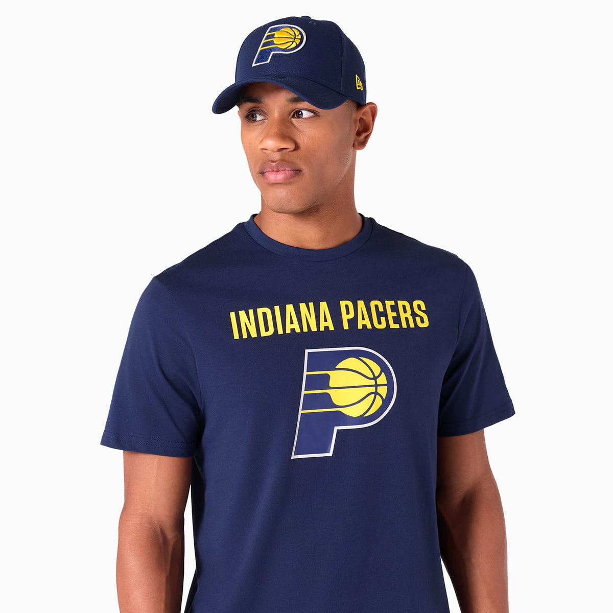 New Era Indiana Pacers NBA Graphic Navy T-Shirt, on-model view showing the navy shirt with INDIANA PACERS in yellow across the chest, a large graphic of the team logo below, paired with a navy cap featuring a raised team logo on the front.