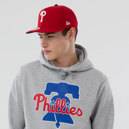 New Era Philadelphia Phillies MLB Grey Pullover Hoodie, on-model view featuring the grey hoodie with a large blue and red Phillies logo on the chest, model wearing a red cap with a white embroidered 'P' and a raised New Era logo on the side.