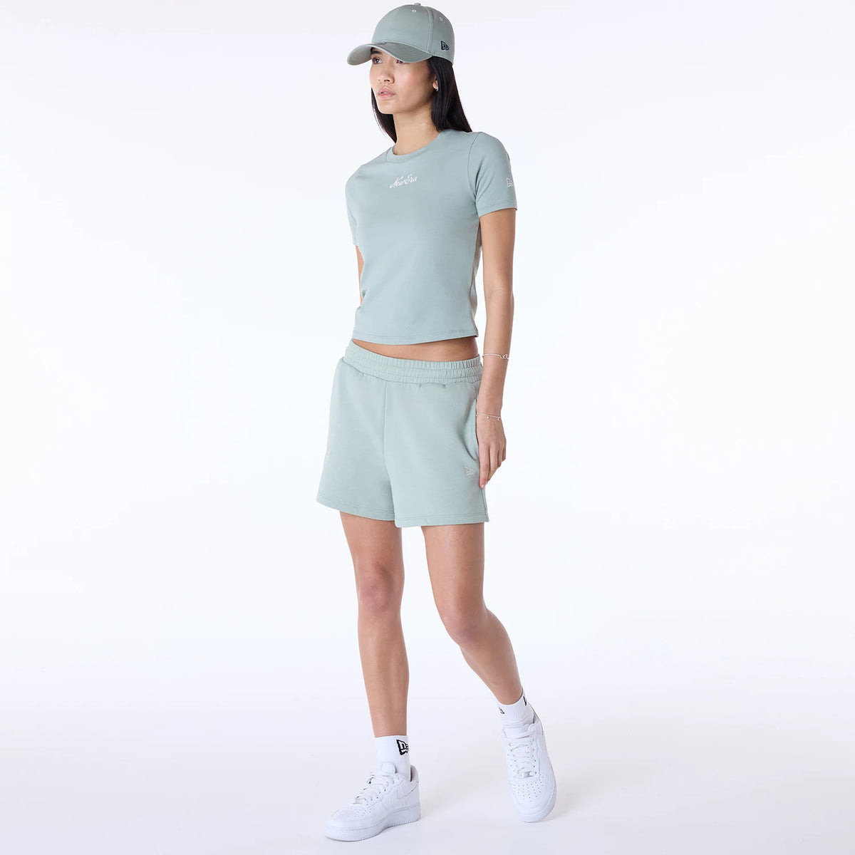 Womens New Era Slim Pastel Blue T-Shirt, on-model view showing a woman wearing a pastel blue T-shirt with a white debossed logo on the chest, matching blue shorts, a pastel blue cap, and white sneakers with a black New Era logo.