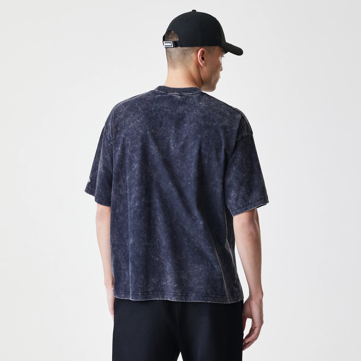 New Era Las Vegas Raiders Sport Classic Black T-Shirt, on-model rear view showing the faded black fabric with short sleeves and a relaxed fit, paired with a black cap featuring a debossed logo on the back.