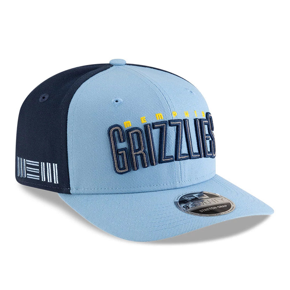 Memphis Grizzlies NBA Statement Pastel Blue New Era 9SEVENTY Stretch Snap Adjustable Cap, three-quarter view showing raised navy and yellow embroidery on the front panel, navy side panels with stripe detailing, and a 9SEVENTY size sticker on the pastel blue visor.
