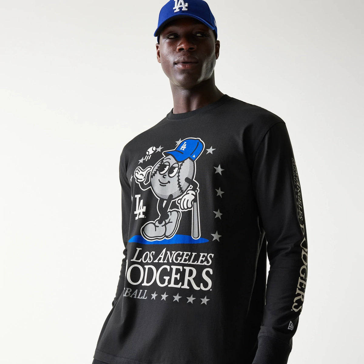 New Era LA Dodgers MLB Character Black Long Sleeve T-Shirt, on-model view featuring a large graphic of a baseball character with an LA cap on the front, the Los Angeles Dodgers text with stars below, and a New Era logo on the left sleeve.