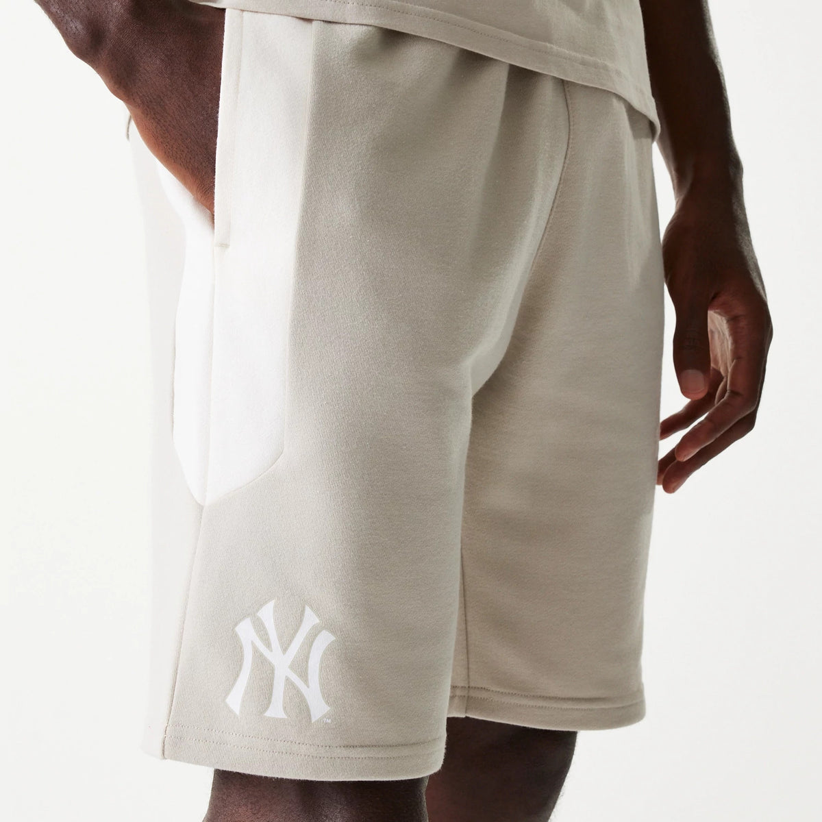 New Era New York Yankees MLB Raglan Cream Shorts, side view showing cream shorts with an elastic waistband and side pocket, featuring a white embossed New York Yankees logo on the lower front side above the hem.