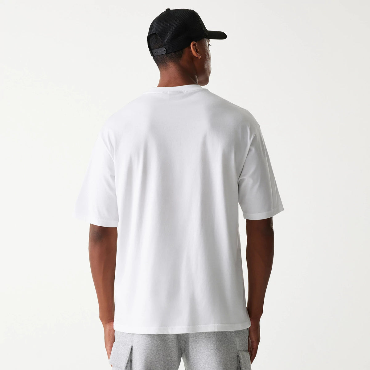 New Era Chicago Bulls NBA Team Graphic White Oversized T-Shirt, rear view showing the plain white back of the oversized t-shirt with short sleeves, and a black mesh cap with a debossed logo worn by the model.