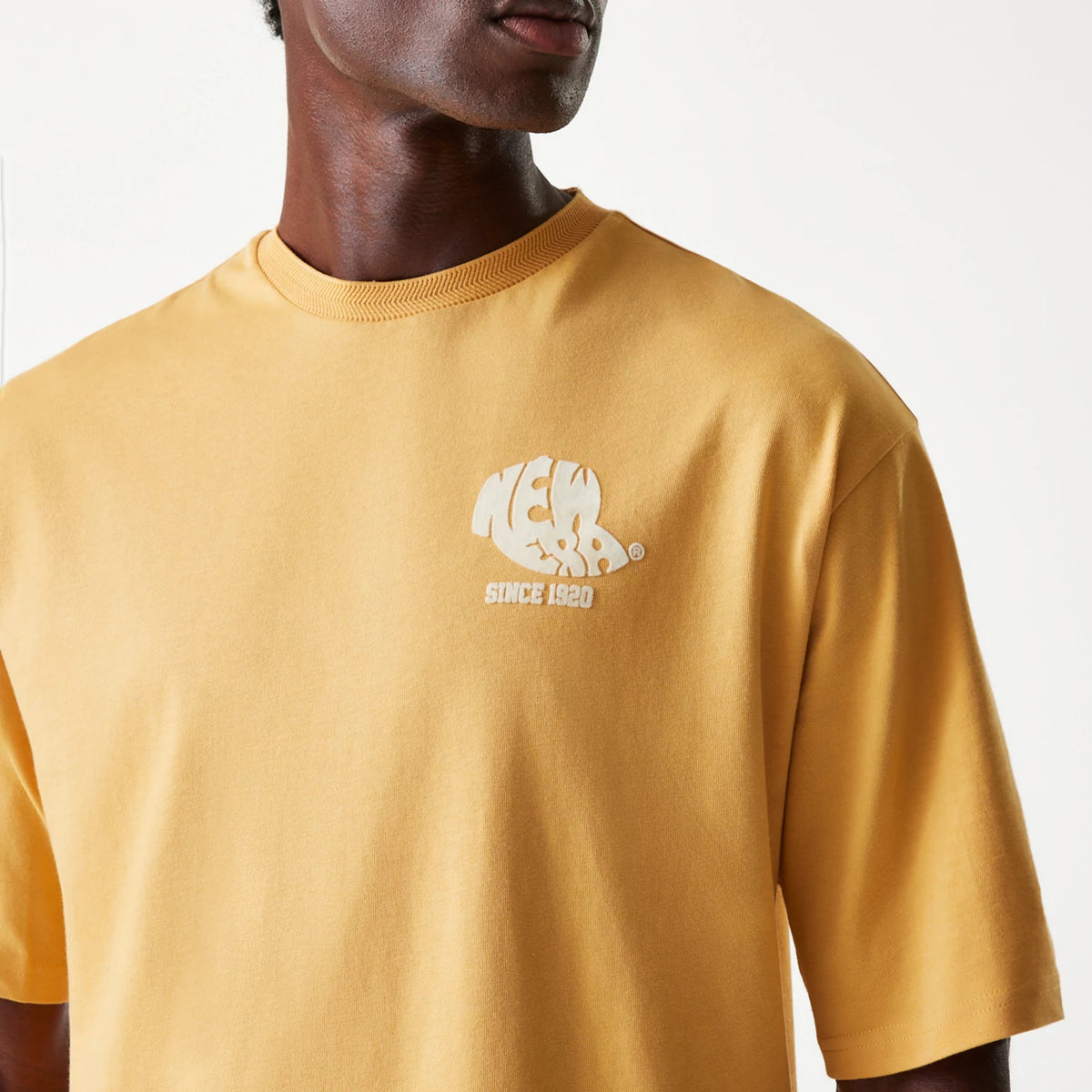 New Era Graphic Beige Oversized T-Shirt, front view featuring a beige oversized shirt with a rounded neckline and a white embossed New Era logo and Since 1920 text on the left chest side.