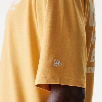New Era Graphic Beige Oversized T-Shirt, side view showing the short sleeve with a white embroidered New Era logo near the hem and part of the large white graphic text printed on the back.