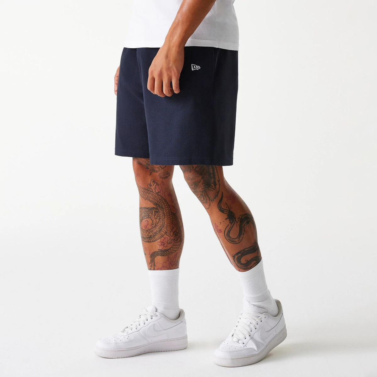 New Era New York Yankees MLB Pique Navy Shorts, on-model view showing the navy shorts worn with white socks and trainers, a raised New Era logo embroidered near the pocket on the front left side.