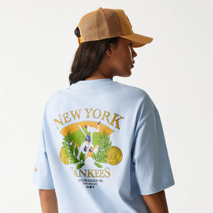New Era New York Yankees MLB Baseball Graphic Pastel Blue Oversized T-Shirt, on-model view showing the back graphic with baseball imagery and typography in gold, green and white on a light blue background.