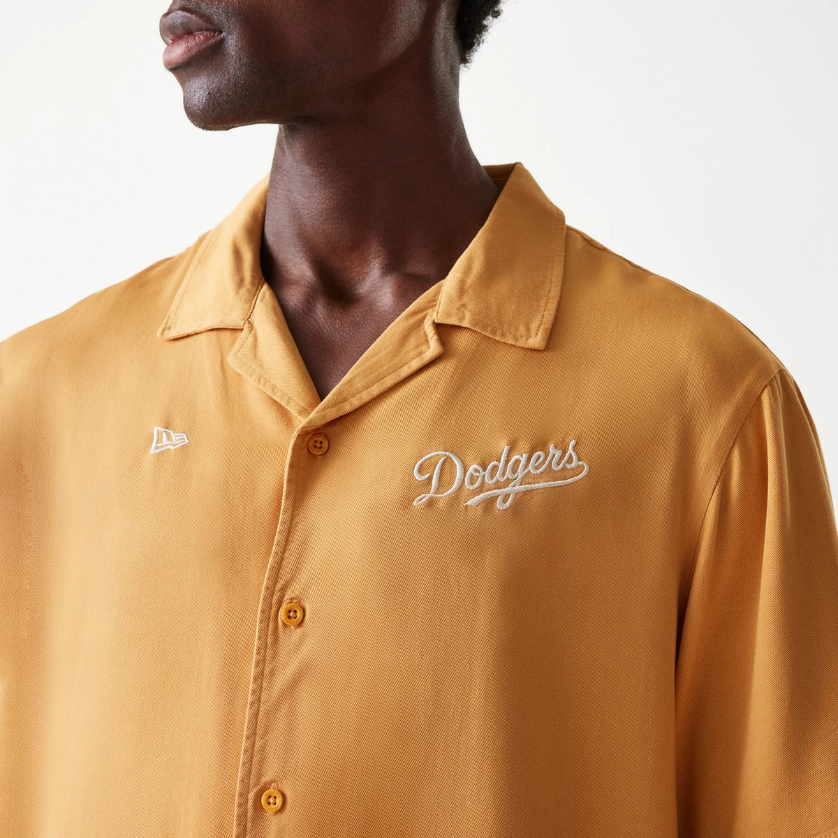 New Era LA Dodgers MLB Graphic Beige Revere Short Sleeve Shirt, on a model highlighting the white scripted Dodgers logo on the left chest and the embroidered New Era flag logo on the right chest above the beige button placket.