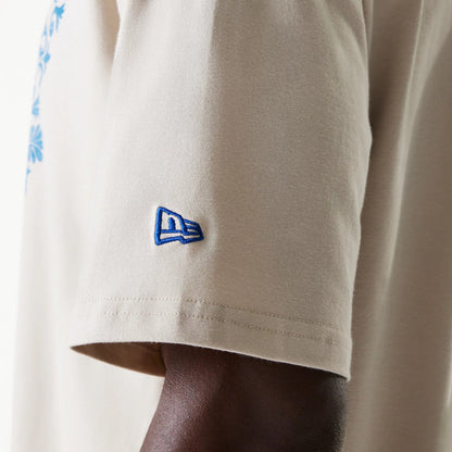 New Era LA Dodgers MLB Floral Graphic Cream Oversized T-Shirt, side view showing a blue embroidered New Era logo on the left sleeve, part of a light cream short sleeve with a glimpse of blue floral pattern on the main body.