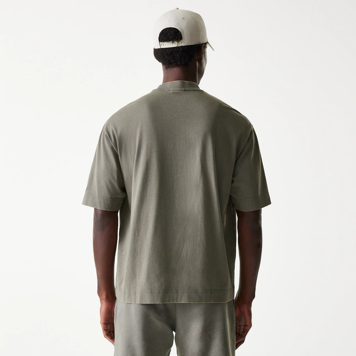 New Era LA Lakers NBA Washed Grey Box T-Shirt, rear view showing the plain grey back of the boxy t-shirt, short sleeves slightly extending over the shoulders, and a cream cap on a person, featuring a row of eyelets on the cap.