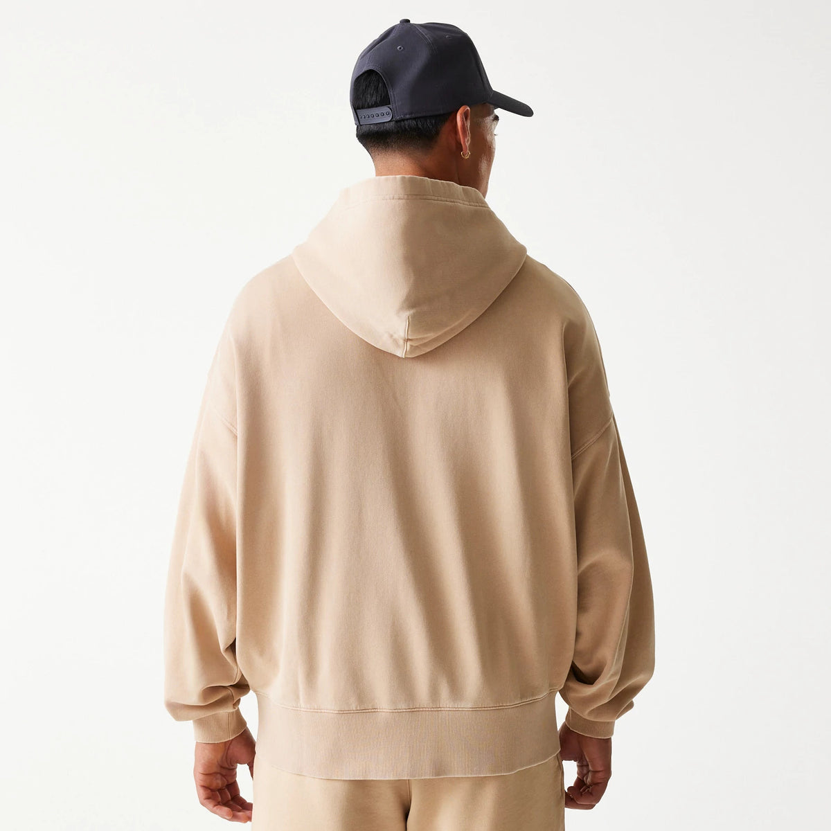 New Era Chicago Bulls NBA Washed Beige Full Zip Hoodie, rear view showing the hood and relaxed fit of the beige fabric, with a clean back design and sleeves extending to the wrists, paired with a black cap.