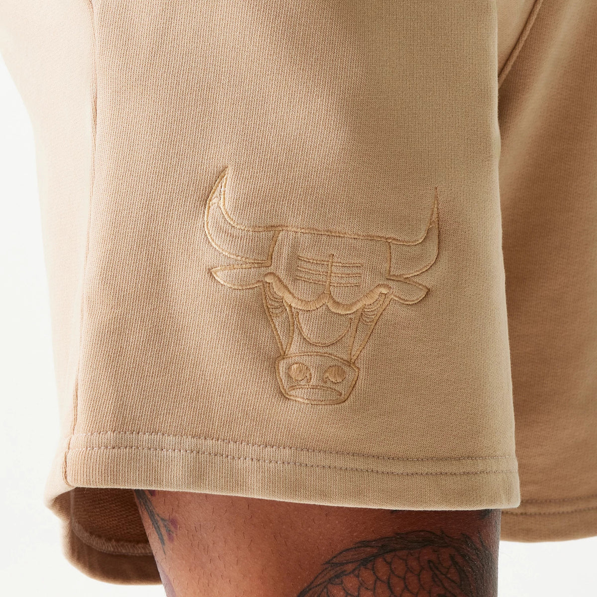 New Era Chicago Bulls NBA Washed Beige Shorts, three-quarter view showing the beige fabric with an embossed Chicago Bulls logo on the lower side and stitching detail along the hem.