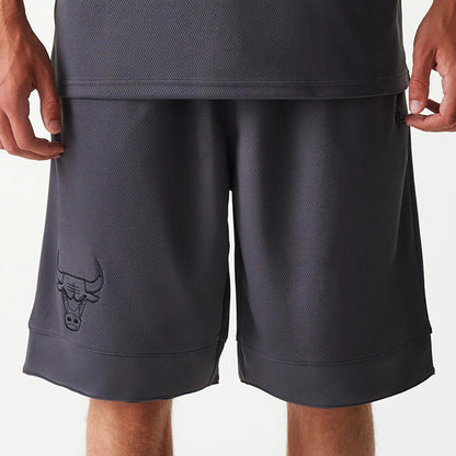 New Era Chicago Bulls NBA Tonal Dark Grey Mesh Shorts, front view showing the dark grey mesh fabric with an embossed Chicago Bulls logo on the lower left leg and a slightly longer hem at the knee.